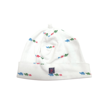A white knit baby beanie hat with a small repeating pattern of colorful turtles in blue, red, and green, featuring a folded cuff and a small navy brand tag.