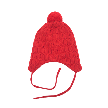 A bright red cable-knit pom-pom beanie hat with ear flaps and long tie strings, shown against a plain white background.