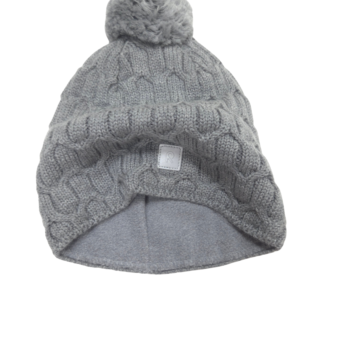 A light gray cable-knit beanie hat with a matching gray faux-fur pom-pom on top and a small white square brand tag on the front. fleece lining