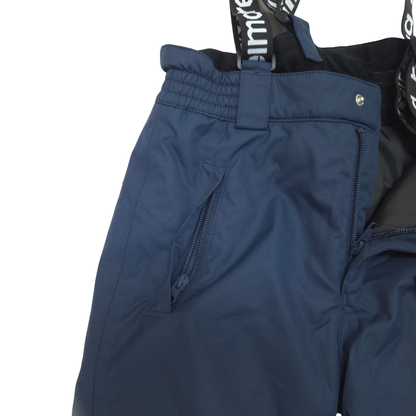 Close-up of dark navy ski pants showing the waistband, side zip pocket, and part of the black bib with white logo text.