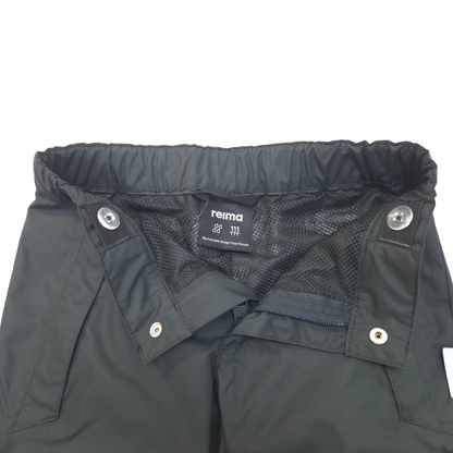 Close-up of the waistband and inner construction of black pants, showing a mesh lining, snap buttons, and a visible Reima brand label.