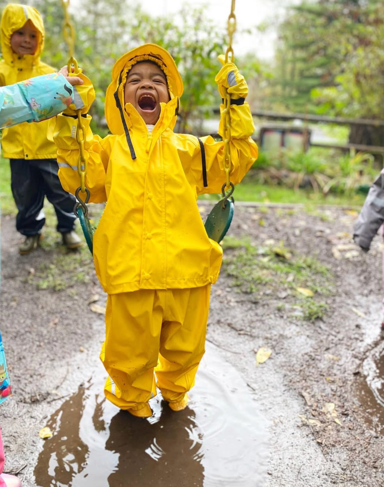 Child in a yellow raincoat playing in a puddle on a rainy day