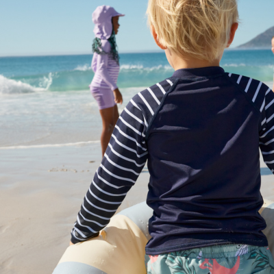 Child wearing a long-sleeve rash guard sitting on a beach with ocean view