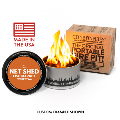 A portable fire pit tin with flames burning inside, shown alongside its branded cardboard box and a round product lid on a white background. Text on the image includes 'Made in the USA' and 'Custom Example Shown.