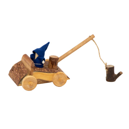 A rustic wooden toy car with a small blue gnome figure inside, shown on a clean white background. The toy features a natural wood body, bark-textured sides, a long wooden handle, and a rope attached to a small dark wood pull.