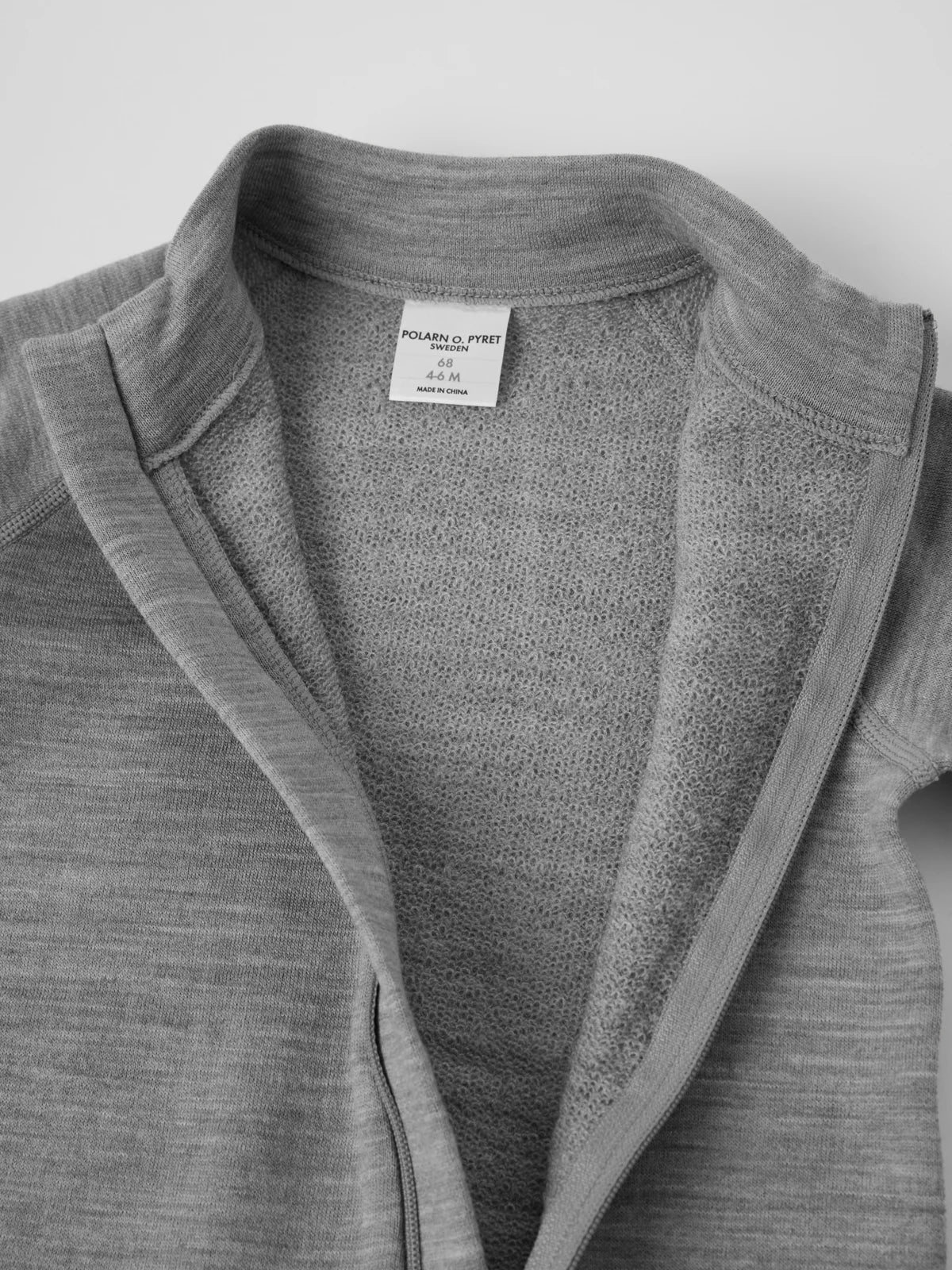 Close-up of a gray knit zip-front merino wool romper with a high ribbed collar and a white interior neck label. 