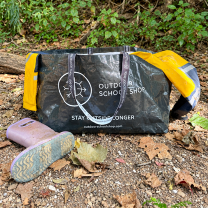 Outdoor School Shop Trunk-Ready Bag holding yellow outdoor gear beside muddy boots at the base of a tree