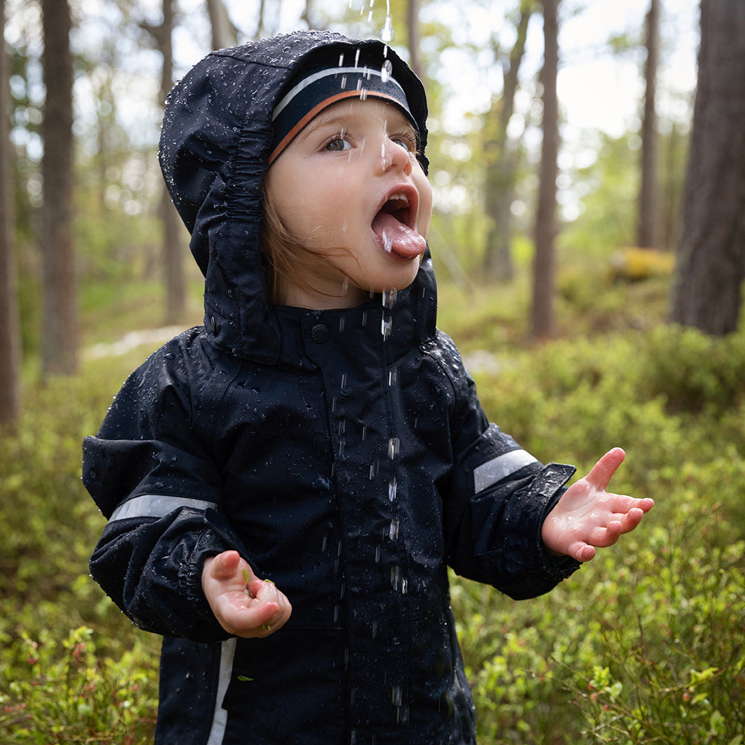 Child in a raincoat standing in a forest, tongue out