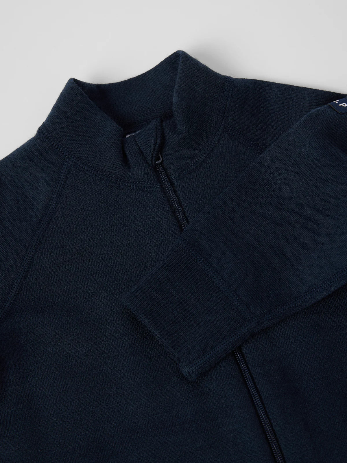 Close-up of a dark navy blue quarter-zip pullover sweater, showing the collar, zipper, and ribbed sleeve cuff against a light gray background. 