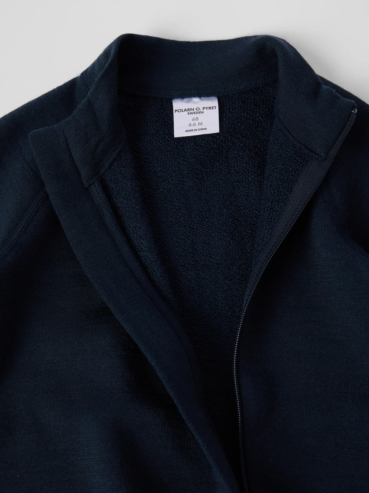 Close-up of a dark navy zip-up jacket with a textured fleece interior lining and a white interior neck label reading polarn o. pyret sweden. 
